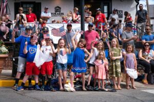 Children wearing red, white, and blue wave American flags along the side of State Street during the Kennett Memorial Day Parade.